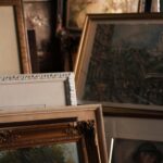 A collection of vintage framed artworks stacked together, showcasing intricate gold and silver frames with delicate details, highlighting a mix of floral and cityscape paintings.