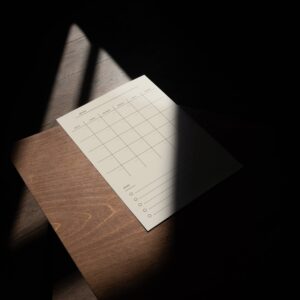 Minimalist beige magnetic planner with a monthly grid and “To Do” list, placed on a wooden surface in dramatic, partial sunlight.