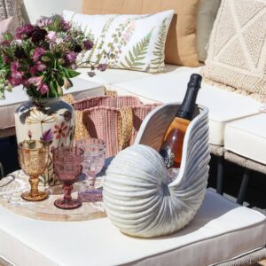 SEA SHELL Vase by Vintelio used as a stylish champagne cooler, displayed on a patio table with pink and amber glasses, floral arrangement, and botanical cushions