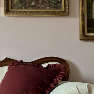 Ballerina Velvet Pillow Case in a luxurious deep burgundy color with elegant ruffled edges, featured on a classic wood-framed, cream-upholstered sofa. Accompanied by a pale velvet round cushion and complemented by vintage gold-framed artwork on a soft pastel wall, perfect for sophisticated, vintage-inspired, and luxury home décor styling. Ideal decorative accent for living rooms, bedrooms, or sitting areas.