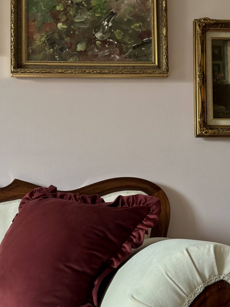Ballerina Velvet Pillow Case in a luxurious deep burgundy color with elegant ruffled edges, featured on a classic wood-framed, cream-upholstered sofa. Accompanied by a pale velvet round cushion and complemented by vintage gold-framed artwork on a soft pastel wall, perfect for sophisticated, vintage-inspired, and luxury home décor styling. Ideal decorative accent for living rooms, bedrooms, or sitting areas.