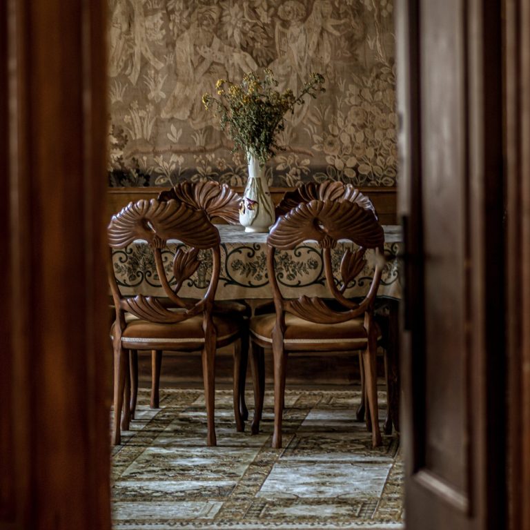 A vertical image of a luxurious dining room with ornate chairs as seen through an open door